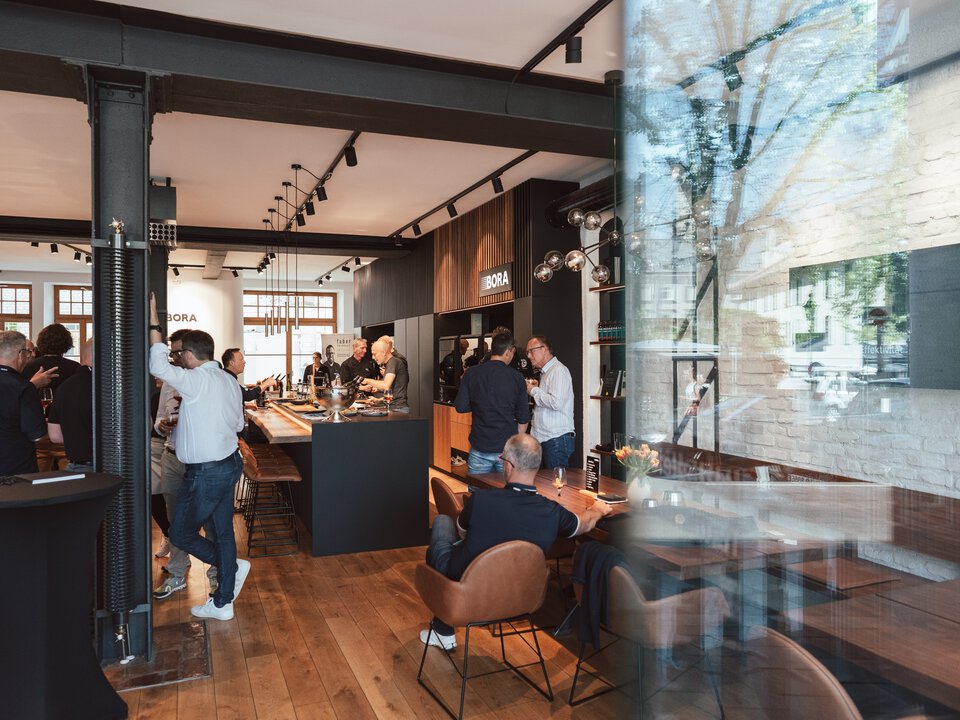BORA Showroom mit Besuchern, modernen Küchen und Dunstabzugssystemen in ansprechendem Ambiente.