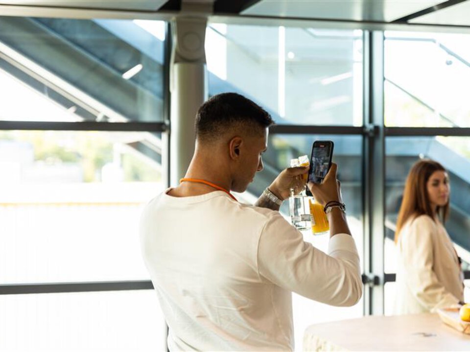 Mann fotografiert Produkt mit Smartphone bei BORA Event in modernem, lichtdurchflutetem Raum.