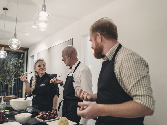 Drei Personen kochen gemeinsam in moderner Küche mit BORA Kochfeldabzug und modernen Pendelleuchten.