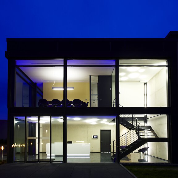 Moderne BORA Glasgebäude-Fassade bei Nacht mit Innenbeleuchtung und klar sichtbarer Treppe und Empfangsbereich.
