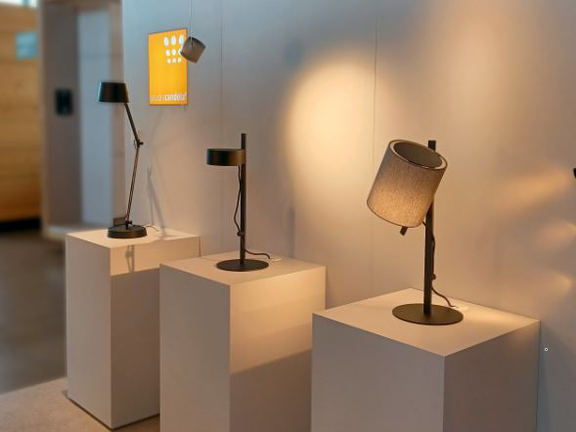 Drei verschiedene BORA Tischlampen auf weißen Podesten in modernem Ausstellungsraum.