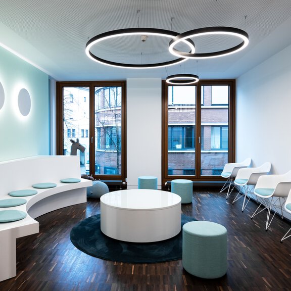 Moderner BORA Wartebereich mit weißer Sitzbank, blauen Sitzhockern und runden LED-Deckenleuchten, Design in hellen Farben.