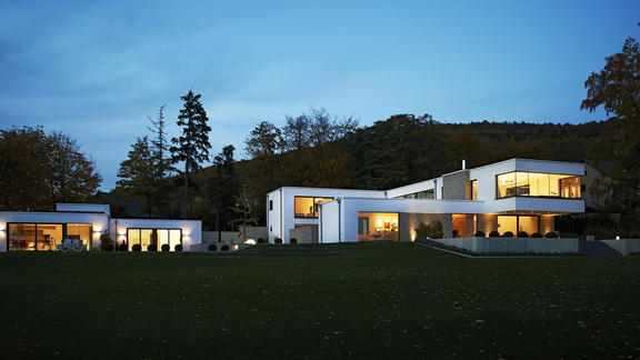 Moderne Architektur bei Dämmerung mit BORA Küchen, große Fensterfronten und stimmungsvolle Beleuchtung im Luxuswohnhaus.