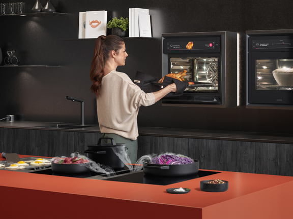 Frau entnimmt gebackenes Gericht aus BORA Backofen, moderne Küche mit BORA Kochfeld und Dunstabzug.