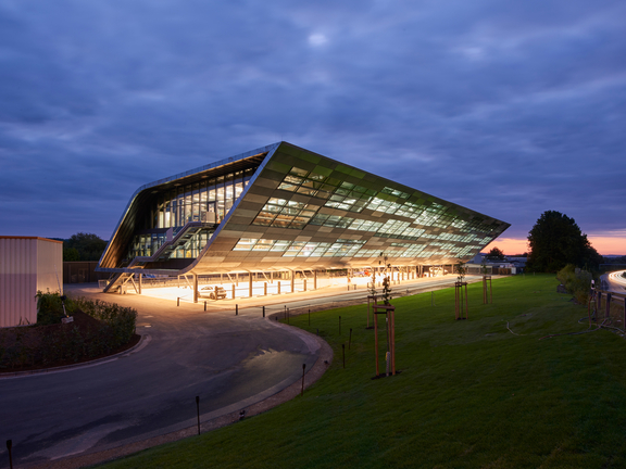 BORA Hauptgebäude bei Abenddämmerung mit beleuchteter Glasfassade und modernem, futuristischem Design.