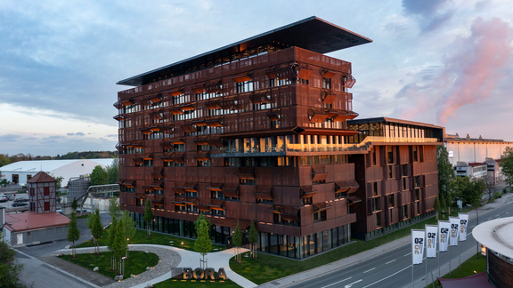 Moderne BORA Firmenzentrale mit rostbrauner Fassade in Lienz, Sunlight-Reflexion am Abendhimmel sichtbar.