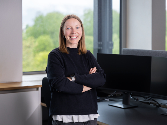 Frau steht selbstbewusst vor BORA Arbeitsplatz mit zwei großen Monitoren und moderner Büroausstattung.