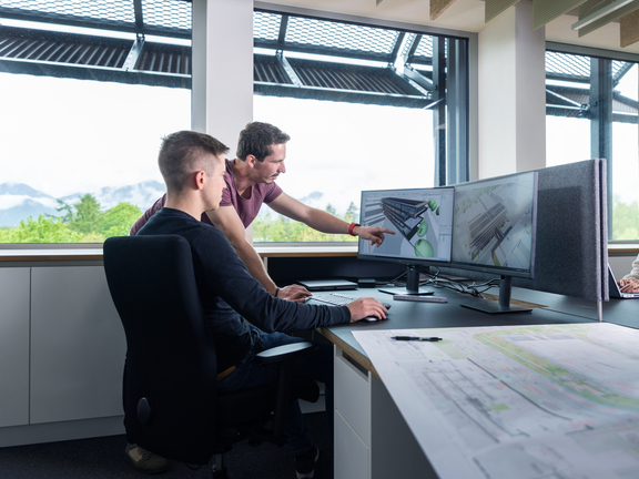 BORA Mitarbeiter arbeiten gemeinsam an CAD-Entwürfen an mehreren Monitoren in hellem Büro mit Blick ins Grüne.