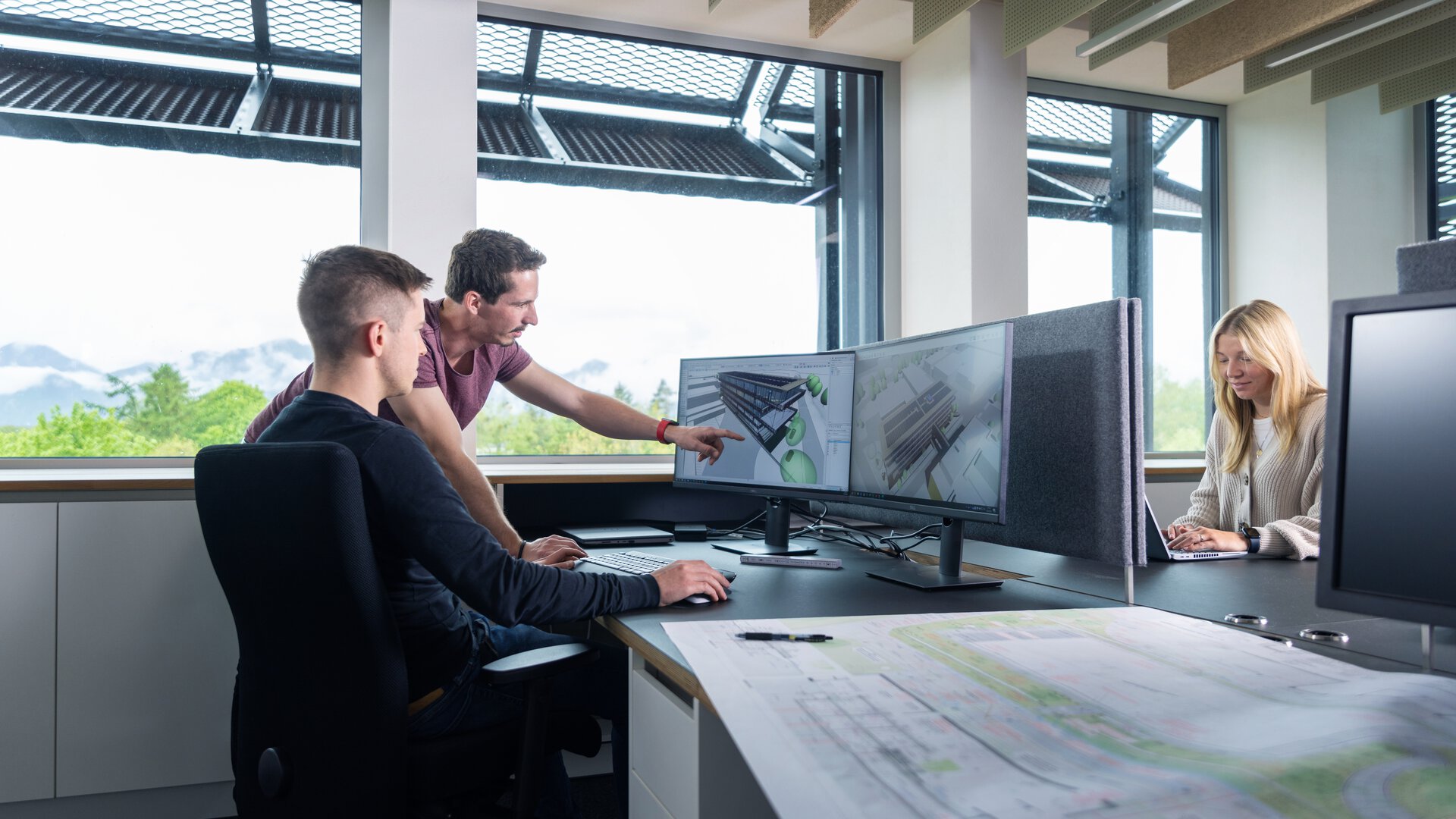 BORA Mitarbeiter arbeiten gemeinsam an CAD-Entwürfen an mehreren Monitoren in hellem Büro mit Blick ins Grüne.