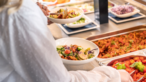 Person nimmt frischen Salat an BORA Buffet mit verschiedenen Beilagen und hochwertiger Präsentation.