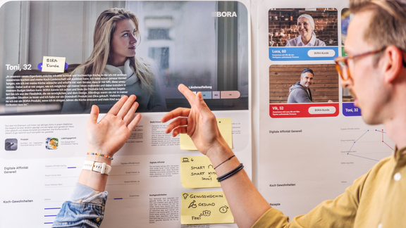 Zwei Personen analysieren BORA Persona-Plakate für Nutzerprofile und Marketingstrategien in einem modernen Büro.