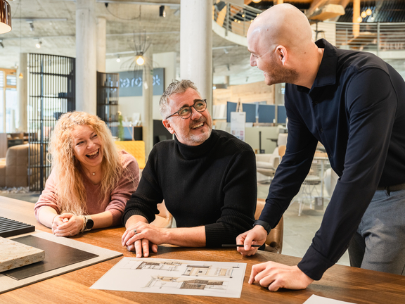 Drei Personen besprechen BORA Küchendesign-Pläne an einem Holztisch im modernen Showroom.