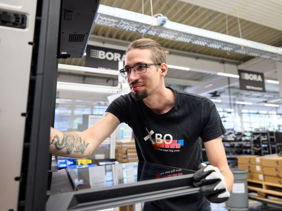 Mitarbeiter montiert BORA Kochfeldabzug in moderner Produktionsumgebung mit BORA Branding.