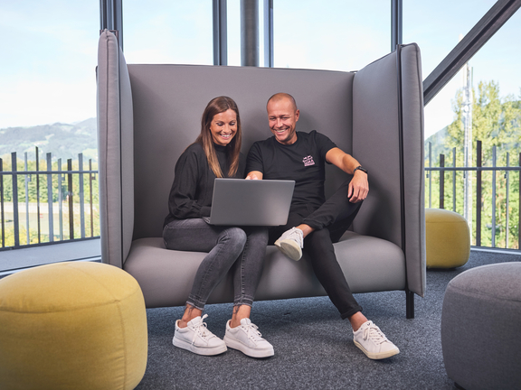 Zwei Personen nutzen Laptop in moderner BORA Lounge mit Schalensofa und Ausblick auf grüne Landschaft.