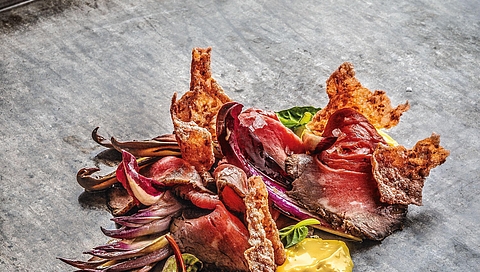 Carne asada con achicoria roja guisada, crema de curry y arroz inflado