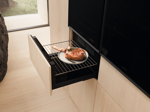 BORA Backofen-Schublade mit gebratenem Fleisch auf Teller, moderne Küchenlösung für warmgehaltenes Essen.