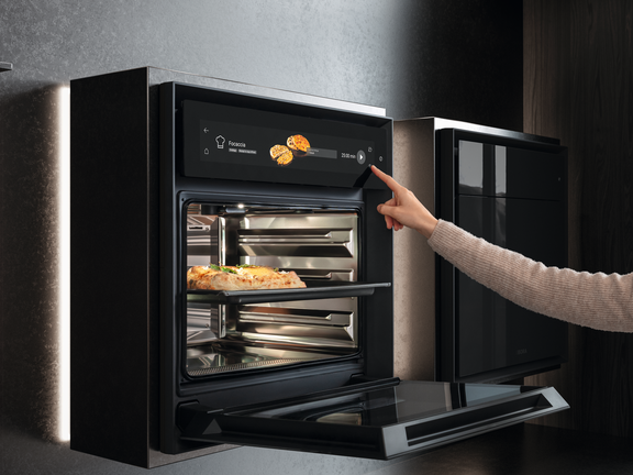 BORA Combi-Dampfgarer in moderner Küche, Hand bedient digitales Touchdisplay, Backgut im Garraum sichtbar.
