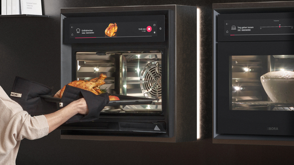 BORA Backofen mit digitalem Display, beim Herausnehmen eines gebratenen Hähnchens. BORA Backofen mit digitalem Display, beim Herausnehmen eines gebratenen Hähnchens.