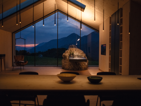 Moderner Wohnraum mit Blick auf Berge und BORA Kochinsel aus Naturstein im Fokus bei Abendlicht.