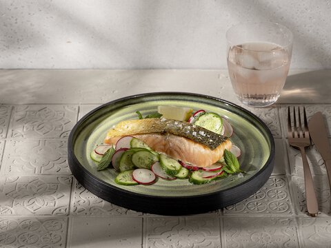 Leckerer Lachs mit Gemüse auf grauem Teller, zubereitet in einer BORA Küche, mit Besteck und Glas Wasser.