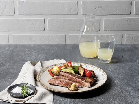 BORA Küchenplatte mit Teller, angerichtet mit Steak und gegrilltem Gemüse, daneben Glas und Karaffe mit Saft.