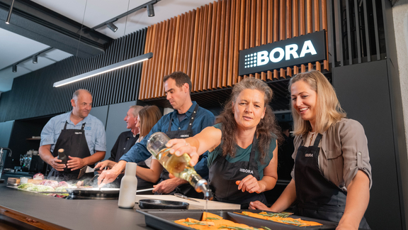 BORA Koch-Event mit mehreren Teilnehmern, die gemeinsam in moderner Küche Speisen zubereiten. BORA Koch-Event mit mehreren Teilnehmern, die gemeinsam in moderner Küche Speisen zubereiten.