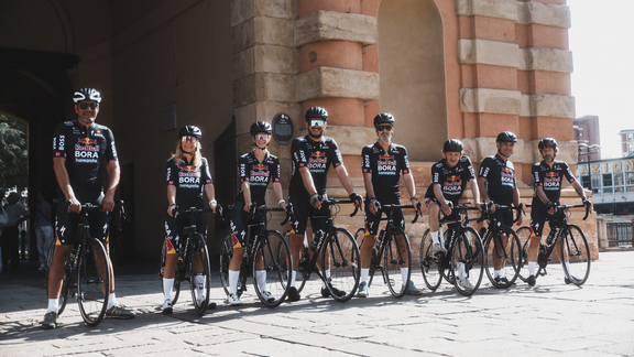 BORA Profi-Radsportteam in Teamkleidung mit Rennrädern vor historischem Gebäude bei Sonnenlicht. BORA Profi-Radsportteam in Teamkleidung mit Rennrädern vor historischem Gebäude bei Sonnenlicht.