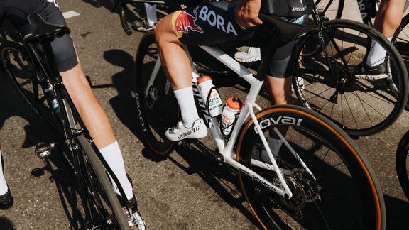 Radfahrer mit BORA-Teamtrikot auf Specialized-Rad mit BORA-Laufrädern, bereit für Rennstart auf Asphalt.