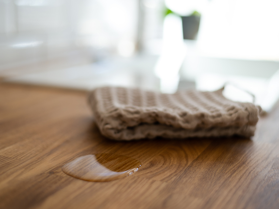 BORA Küchenarbeitsplatte mit Wasserspritzer und grauem Reinigungstuch, zeigt pflegeleichtes Material. BORA Küchenarbeitsplatte mit Wasserspritzer und grauem Reinigungstuch, zeigt pflegeleichtes Material.