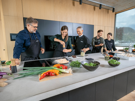 Moderne BORA Kücheninsel mit Induktionskochfeld und Dunstabzug, fünf Personen bereiten gemeinsam frische Speisen zu. Moderne BORA Kücheninsel mit Induktionskochfeld und Dunstabzug, fünf Personen bereiten gemeinsam frische Speisen zu.